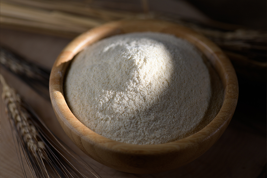 Mąka żytnia jasna w drewnianej misce, w tle kłosy zboża.