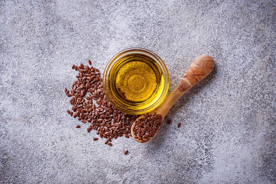 Olej lniany tłoczony na zimno w szklanej misce z nasionami lnu na drewnianej łyżce, na szarym tle teksturowanym